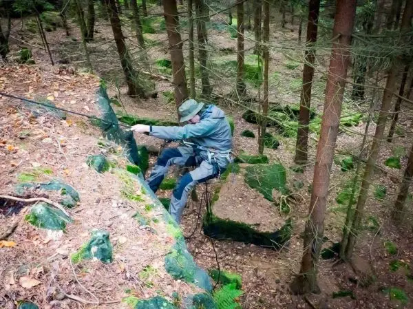 Seilquerung an einer Felswand im Wald mit Kletterausrüstung