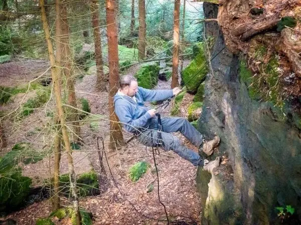 Seilquerung an einer Felswand im Wald mit Kletterausrüstung