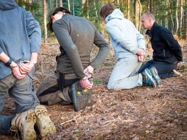 Vier Personen knien im Wald mit Handschellen hinter dem Rücken