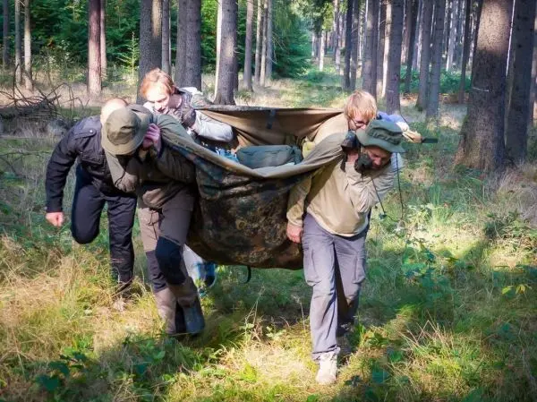 Vier Personen tragen eine improvisierte Trage durch den Wald