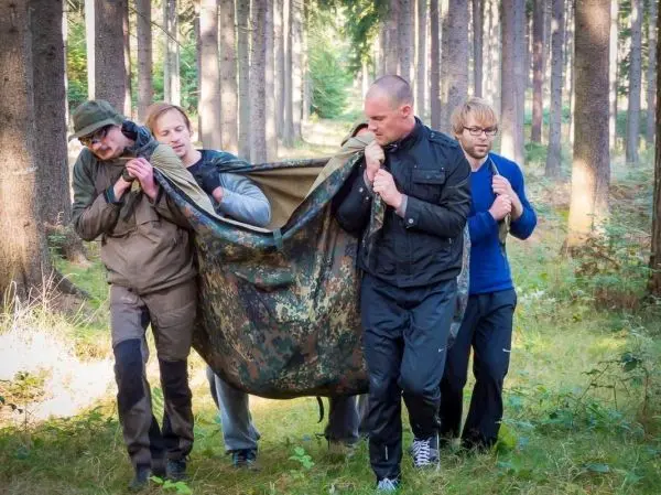 Vier Personen tragen eine improvisierte Trage durch den Wald