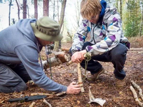 Zwei Personen bauen eine selbstgebaute Konstruktion aus Ästen im Wald