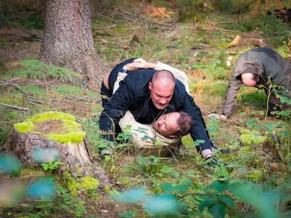 Zwei Personen im Wald, eine Person hält die andere am Boden fest
