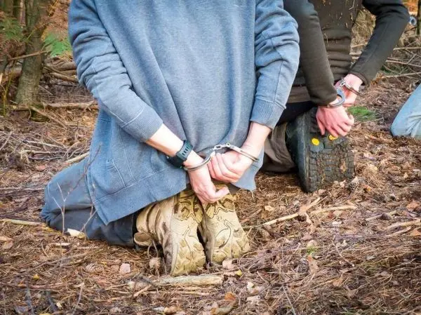 Zwei Personen knien mit Handschellen hinter dem Rücken im Wald