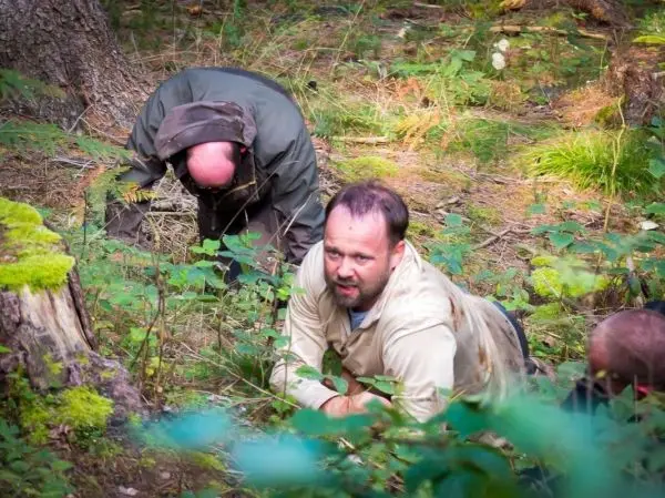 Zwei Personen kriechen durch den Wald, umgeben von Pflanzen und Moos