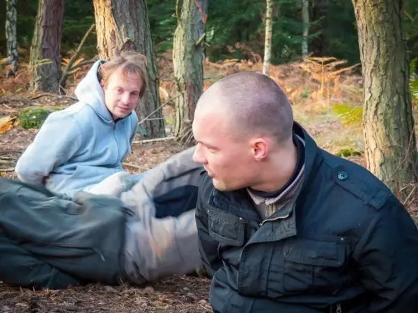 Zwei Personen sitzen im Wald auf dem Boden zwischen Bäumen