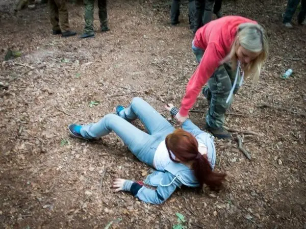 Eine Person hilft einer anderen, die am Boden liegt, in einem Waldgebiet