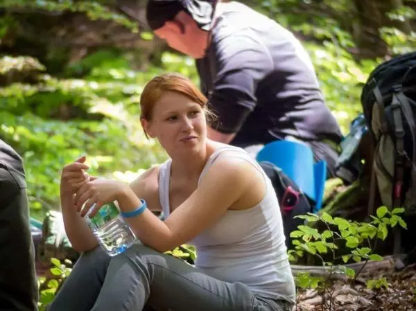 Eine Person sitzt im Wald und hält eine Wasserflasche in der Hand