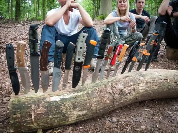Eine Reihe von Messern steckt in einem umgedrehten Baumstamm im Wald