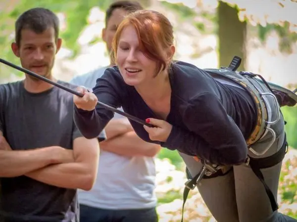 Frau mit Klettergurt und Seil in der Luft, beobachtet von zwei Personen