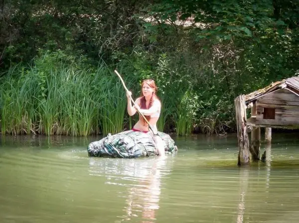 Frau paddelt mit einem Stock auf einem improvisierten Floß im Wasser