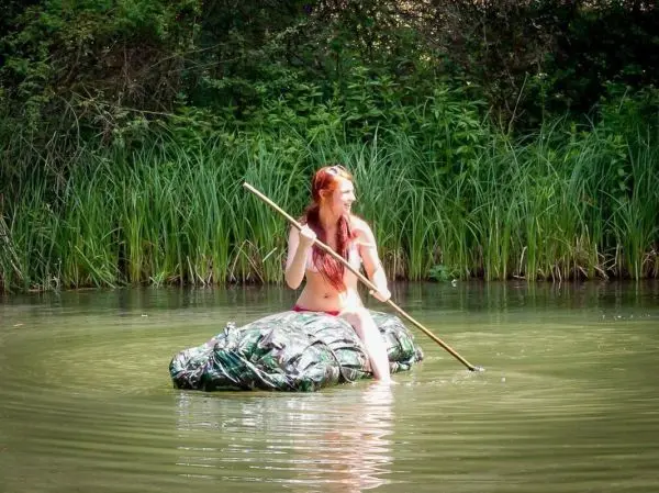 Frau paddelt mit einem Stock auf einem improvisierten Floß im Wasser