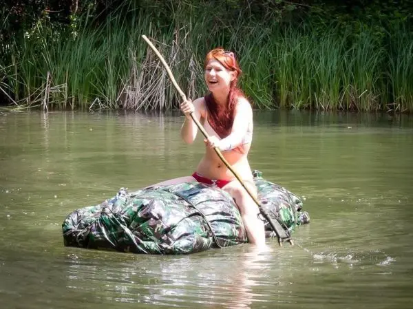 Frau sitzt auf einem camouflagefarbenen Floß und hält einen Stock in der Hand