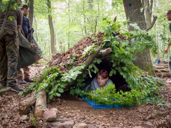 Frau sitzt in einer Tarp-Notunterkunft, während andere Materialien sammeln