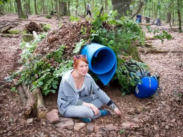 Frau sitzt vor einer improvisierten Tarp-Notunterkunft aus Ästen und Blättern