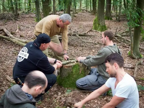 Fünf Personen arbeiten gemeinsam an einer Holzarbeit auf einem Baumstumpf im Wald