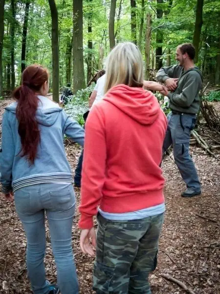 Gruppe arbeitet an einer Holzstruktur im Wald, einige Personen stehen in der Nähe