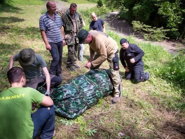 Gruppe arbeitet an einer improvisierten Trage aus einer grünen Plane im Freien