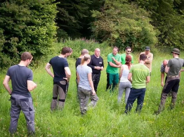 Gruppe diskutiert im Freien, umgeben von hohem Gras und Bäumen