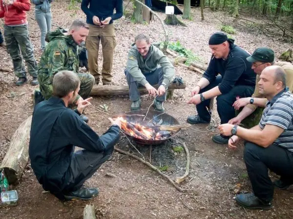 Gruppe sitzt um ein Feuer und röstet Essen auf langen Stöcken