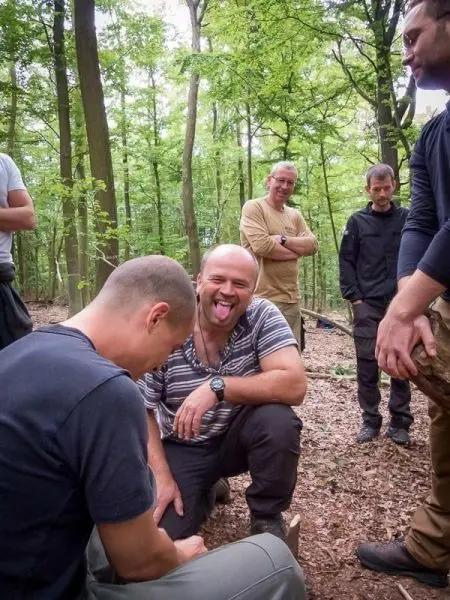 Gruppe von Personen in einem Wald, einige beobachten einen anderen, der auf dem Boden sitzt