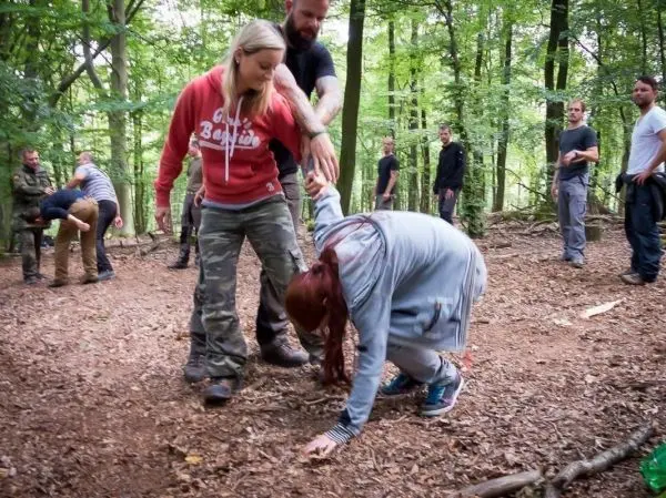 Gruppendynamik im Wald, eine Person kniet am Boden, andere helfen