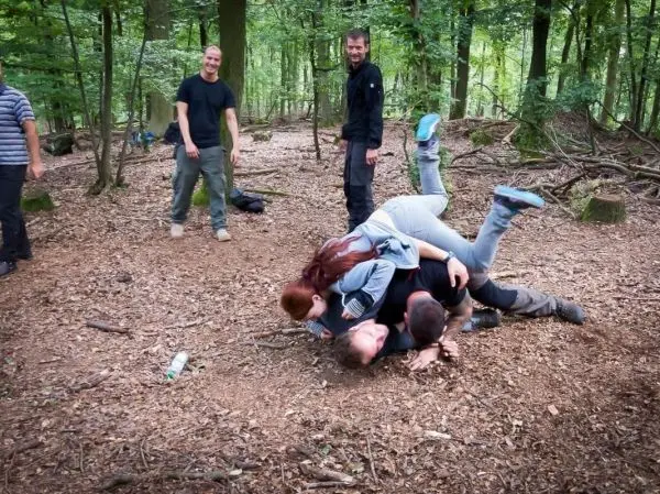 Gruppendynamik im Wald, mehrere Personen auf dem Boden in einer spielerischen Auseinandersetzung