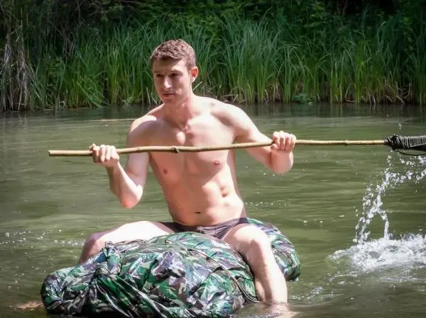Junge paddelt auf improvisiertem Floß mit einem Stock im Wasser