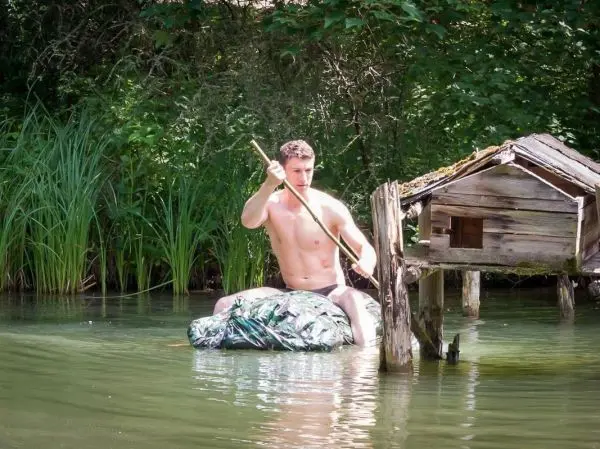 Junge paddelt mit einem Stock auf einem improvisierten Floß im Wasser