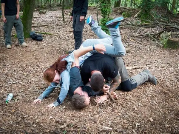 Kampftraining am Boden zwischen mehreren Personen im Wald auf Laub