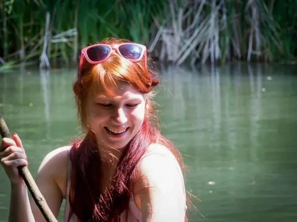 Lächelnde Person hält einen Stock am Ufer eines Gewässers