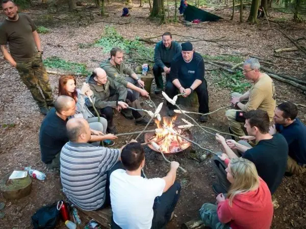 Lagerfeuer in einem Wald mit mehreren Personen, die Stockbrot rösten