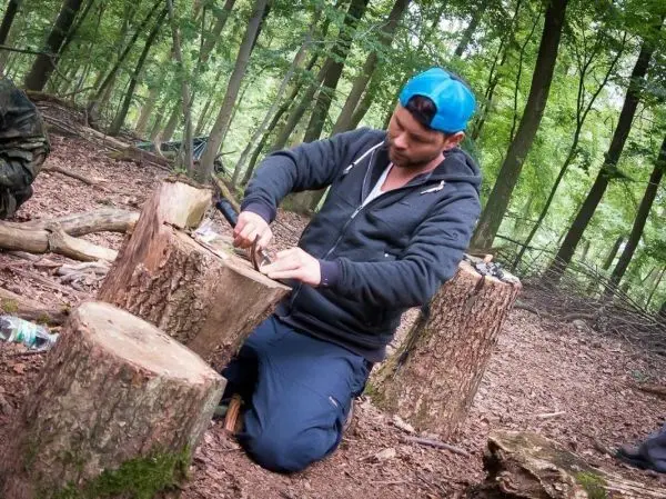 Mann bearbeitet Holzstück mit einem Messer im Wald