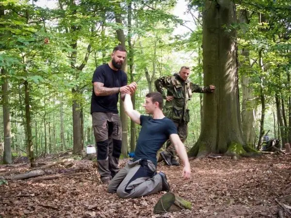 Mann hilft sitzendem Mann beim Aufstehen im Wald