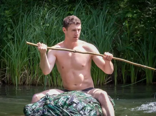 Mann paddelt auf improvisiertem Floß mit einem Stock im Wasser