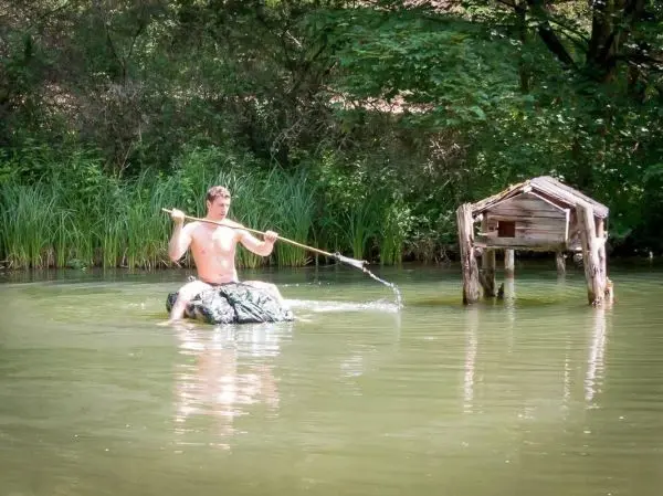 Mann sitzt auf improvisiertem Floß und fischt mit einem Stock im Wasser