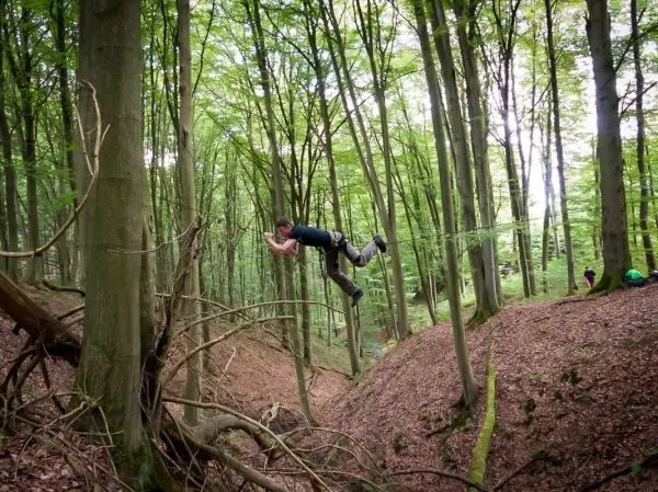 Mann überquert eine Schlucht mit einer selbstgebauten Seilbrücke zwischen Bäumen