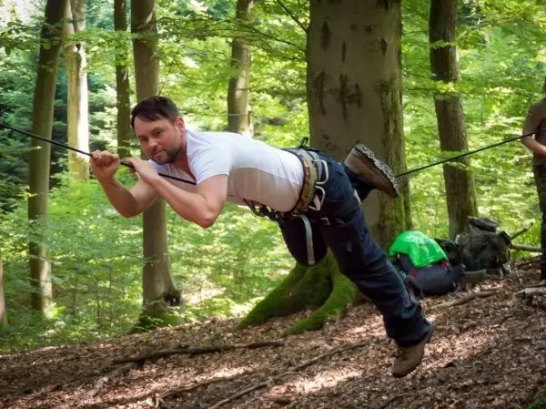 Mann überquert eine selbstgebaute Seilbrücke im Wald