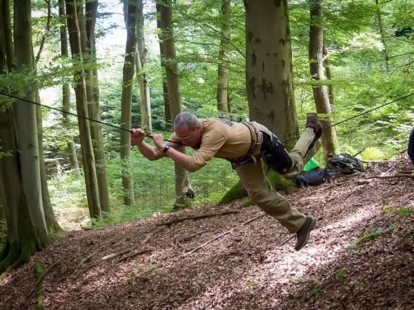 Mann überquert eine selbstgebaute Seilbrücke zwischen Bäumen im Wald