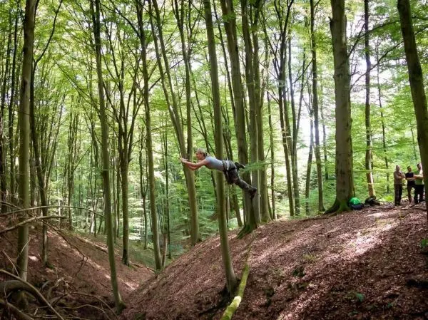 Mann überquert eine selbstgebaute Seilbrücke zwischen zwei Baumstämmen