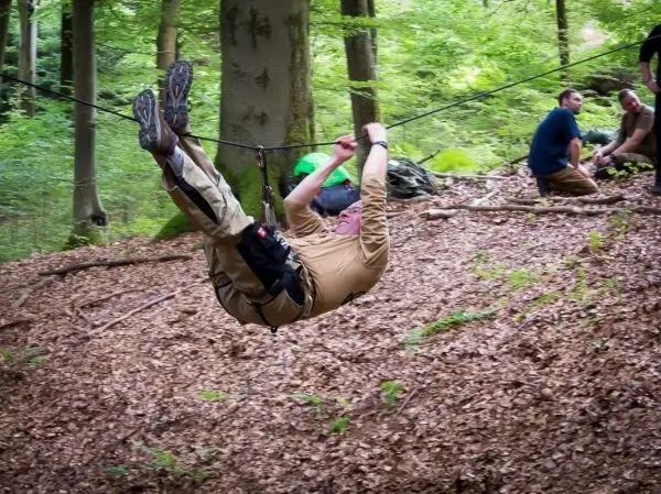 Mann überquert mit einem Karabiner eine selbstgebaute Seilbrücke im Wald