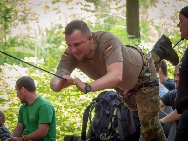 Mann überquert mit Seil eine selbstgebaute Seilbrücke im Wald