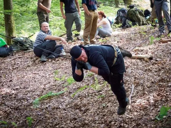 Mann überquert selbstgebaute Seilbrücke im Wald, Zuschauer im Hintergrund