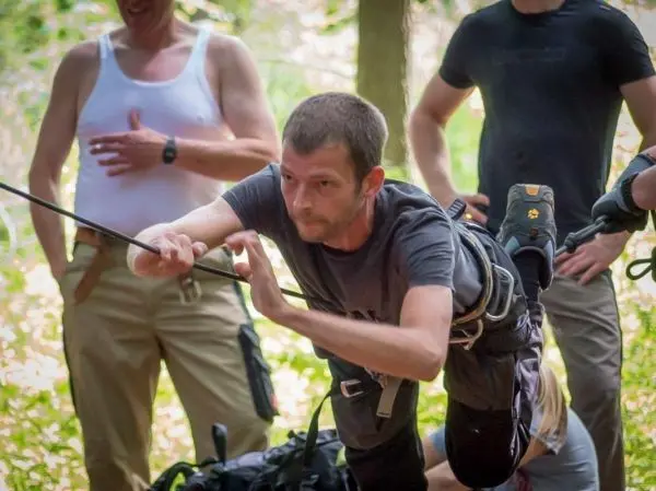 Mann überquert selbstgebaute Seilbrücke mit gesichertem Seil im Wald