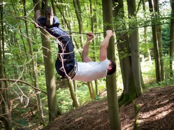 Mann überquert selbstgebaute Seilbrücke zwischen Bäumen im Wald