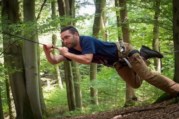 Mann überquert selbstgebaute Seilbrücke zwischen Bäumen im Wald