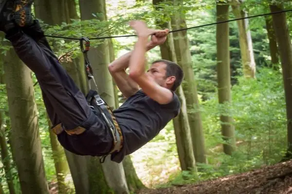 Mann überquert selbstgebaute Seilbrücke zwischen Bäumen im Wald