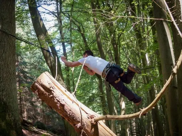 Mann überquert selbstgebaute Seilbrücke zwischen zwei Bäumen