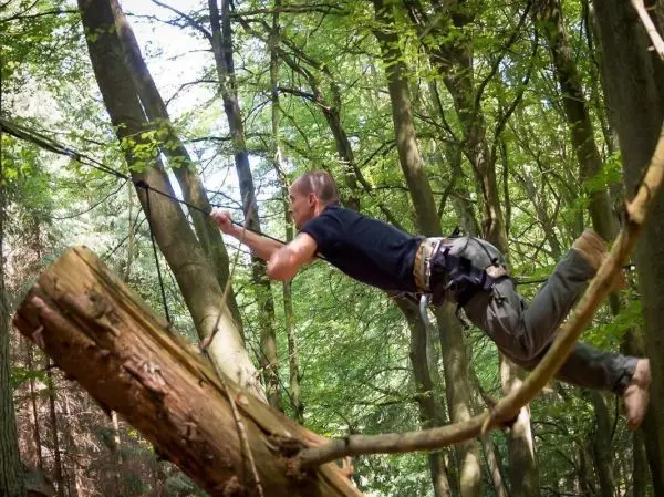 Mann überquert selbstgebaute Seilbrücke zwischen zwei Bäumen