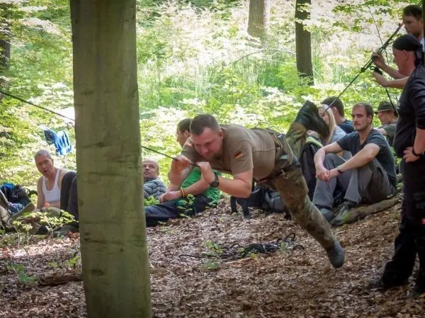 Mann überquert selbstgebaute Seilbrücke zwischen zwei Bäumen im Wald